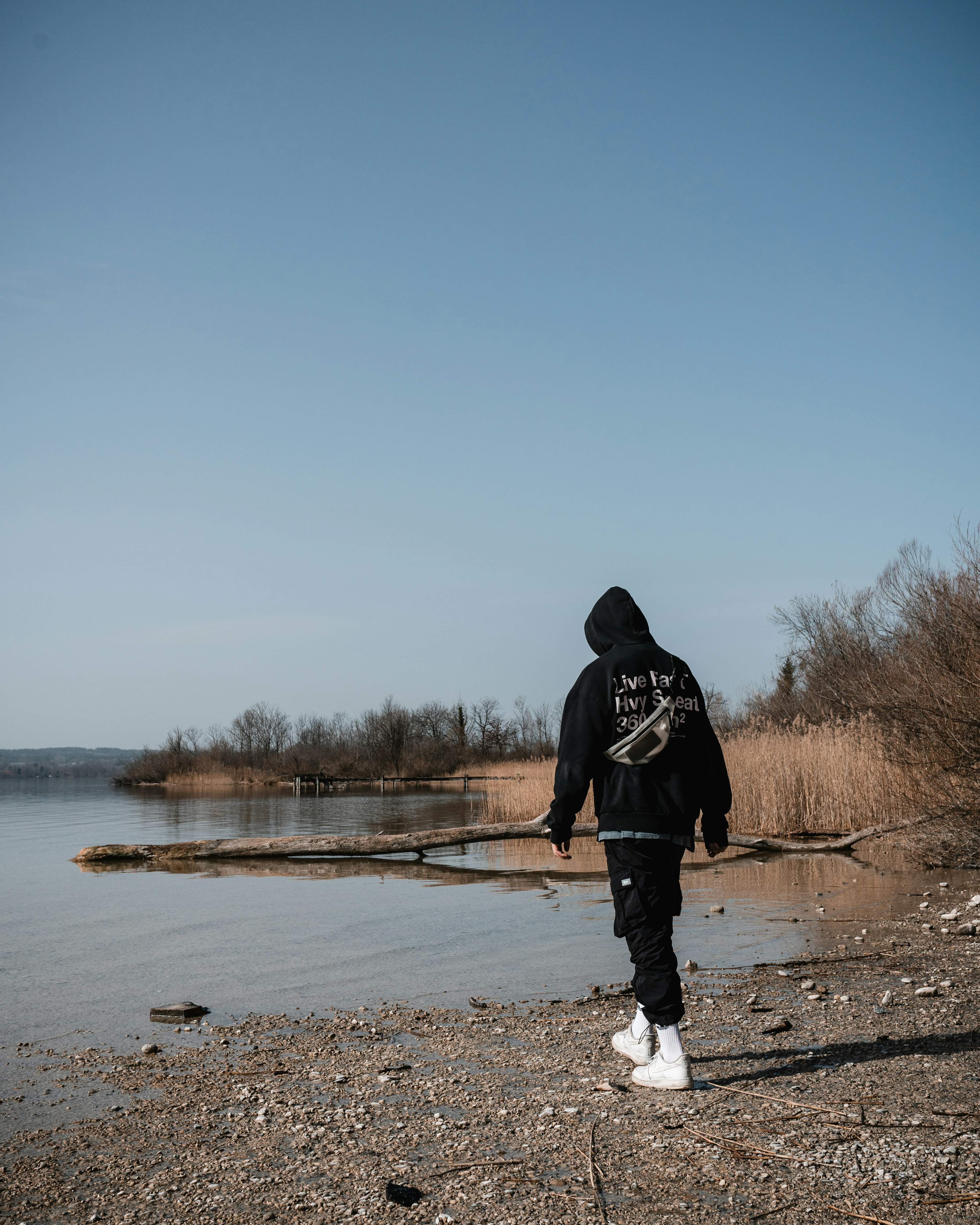 man in black hoodie standing on brown field near lake during daytime